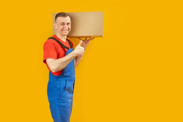 送货员把箱子扛在肩上 竖起大拇指 Courier带来了包裹被黄色背景隔离 复制空间 — 图库照片
