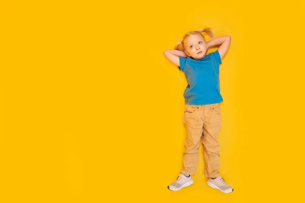 꼬리를 소녀는 티셔츠와 바지를 노란색 배경에 있는아이 위에서 흉내내기 — 스톡 사진