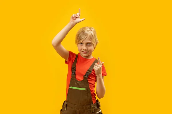Portrét Usměvavého Chlapce Montérkách Ukazujícího Prsty Nahoru Rozumím Žluté Pozadí — Stock fotografie
