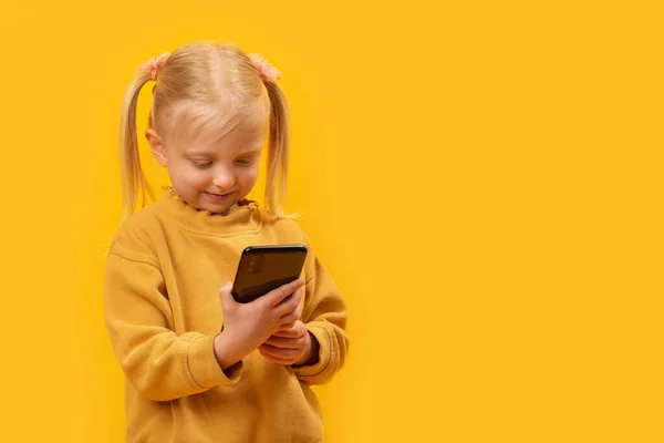 少女は携帯電話で漫画を見ている スマートフォンで子供の肖像画 黄色の背景 スペースのコピー — ストック写真