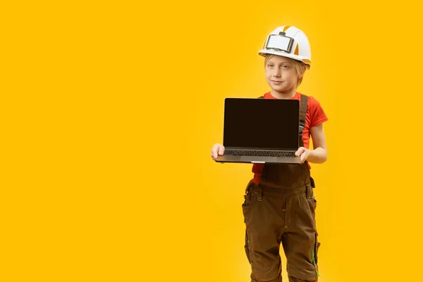 穿着工作服和防护头盔的小男孩拿着装有空屏幕的笔记本电脑 作为建筑师的孩子复制空间 — 图库照片