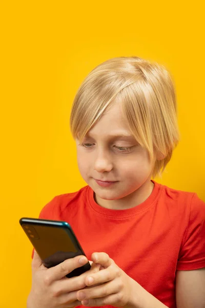 スマートフォンを手に 赤いTシャツを着た金髪の少年の肖像画を閉じます 男性の子供は電話を使う — ストック写真