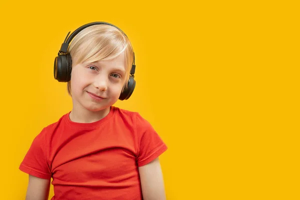 ブロンドの笑顔の学童は大きなヘッドフォンで音楽を聴く 黄色の背景にティーンエイジャーの肖像画 スペースのコピー — ストック写真