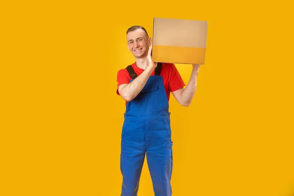 笑顔宅配業者は 黄色の背景に段ボール箱を保持しています 紙箱付きのハンサムな白人デリバリーマンを笑顔 コピースペース モックアップ — ストック写真