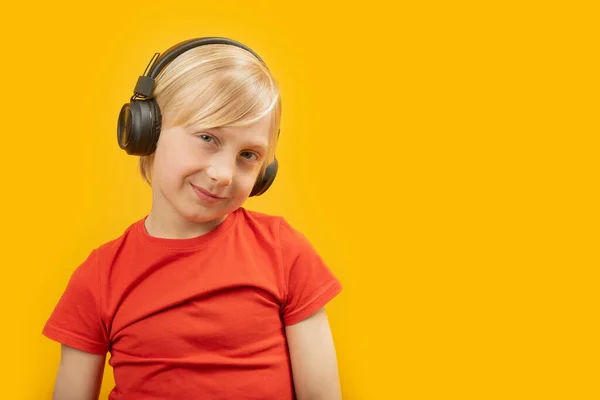 笑顔のブロンドの少年は大きなヘッドフォンで音楽を聴く 黄色の背景にティーンエイジャーの肖像画 スペースのコピー — ストック写真