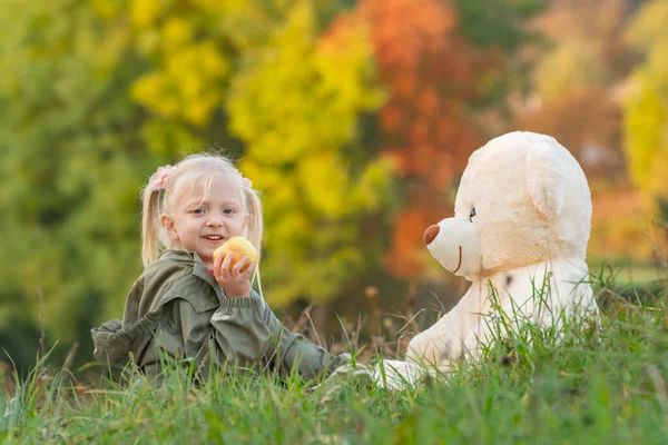 Блондинка Ест Яблоко Играет Большой Мягкой Игрушкой Сидя Траве Ребенок — стоковое фото
