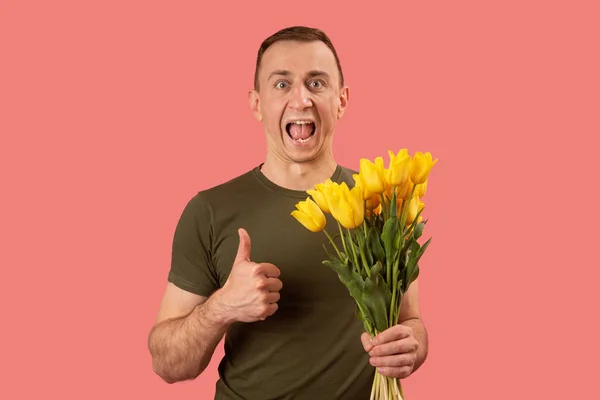 男人拿着一束黄色的郁金香花 竖起大拇指 张大嘴尖叫着 以粉红为背景隔离 — 图库照片