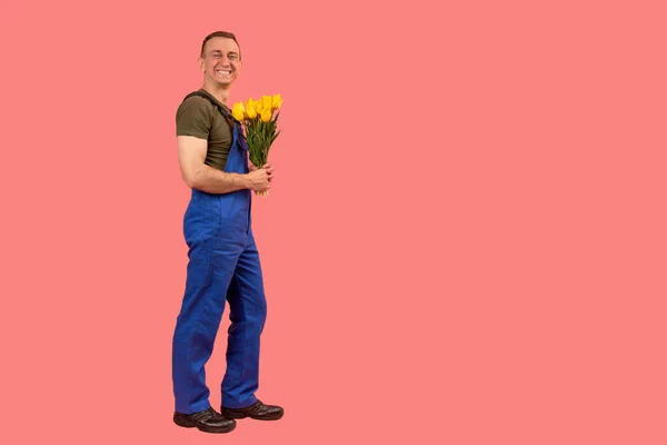 Усміхнений Чоловік Блакитному Комбінезоні Тримає Букет Квітів Рожевий Фон Повнометражний — стокове фото