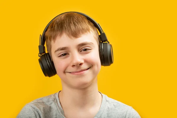 黄色の背景に黒のヘッドフォンで笑顔ブルネットの少年の肖像画を閉じます 十代の若者は音楽やオーディオブックを聞く — ストック写真