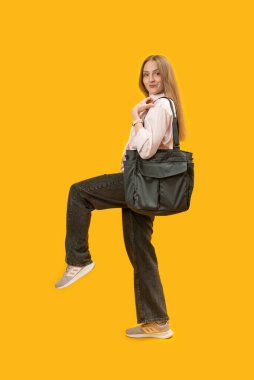 Sarı stüdyo arka planında duran siyah tekstil çantalı kadın. Dikey çerçeve. Boşluğu kopyala