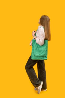 Yeşil çevre dostu alışveriş çantası kızların omzunda. Kadınların dikey çerçeve portresi sarı arka planda tekstil çantası tutuyor