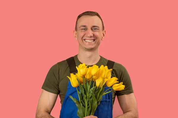 Delivery man with beautiful smile holds bouquet of yellow flowers, pink background. Flowers delivery concept
