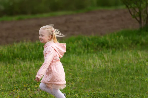 快乐地跑着 年轻的欧洲姑娘 金发碧眼 穿着粉红色的衣服 穿过田野或草地 春天的时间 — 图库照片