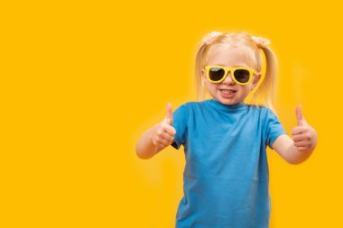 Mavi tişörtlü ve güneş gözlüklü çocuk portresi iki elli bir jest gibi görünüyor. Anaokulu öğrencisi onayladı. Uzayı kopyala, taklit et.