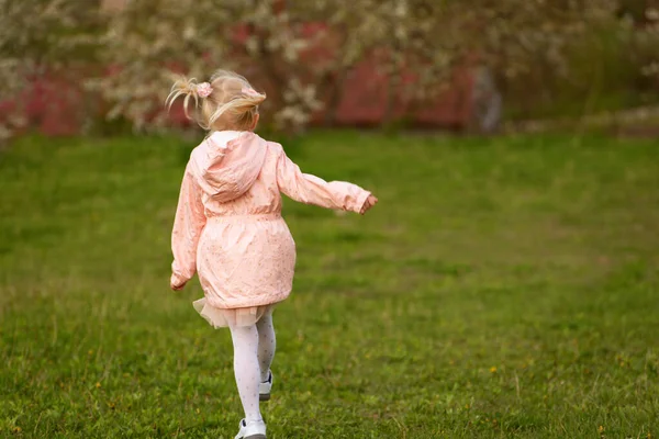 有两条尾巴的金发小女孩穿过公园或绿色的草地 春天的时候 背景色 — 图库照片