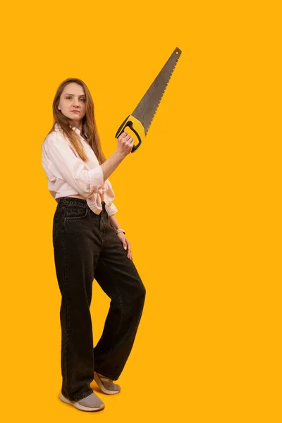 Stüdyoda Sarı Arka Planda Duran Eli Testereli Ciddi Bir Kadın — Stok fotoğraf