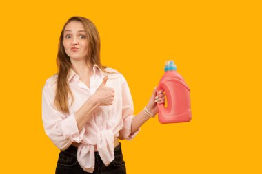 Ev hanımı pembe plastik şişeyi tutuyor ve baş parmağını kaldırıyor. Genç bir kadın ürün reklamı yapıyor. Uzayı kopyala, taklit et