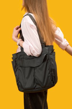 Siyah eko tekstil çantası tutan genç bir kadın tüketici. Sarı arka planda alışveriş torbası olan kızın portresini kapat.