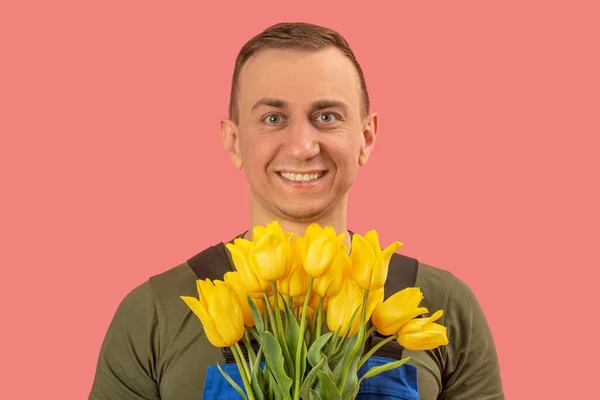 Portrait of smiling young man with bouquet of yellow tulips isolated on pink background. Flowers Delivery