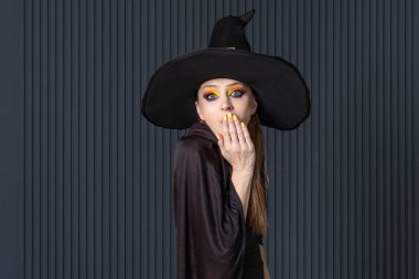 Cadı şapkalı çekici kadın şaşırmış ya da ayartılmış. Parlak makyaj. Mevsimlik indirimler. Cadılar Bayramı indirimi. Koyu arkaplan.