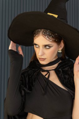 Siyah cadı şapkası takan güzel makyajlı genç seksi bir kadın. Baştan çıkarıcı bakışlı kız. Cadılar Bayramı Kıyafeti.