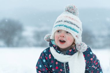 Dışarıda kışın örgü şapkalı küçük beyaz bir çocuk. İki yaşındaki bir çocuğun portresi, açık havada, karlı ve soğuk havada.