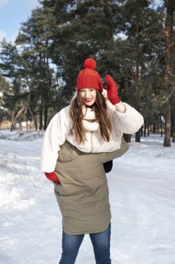 Adamın omzunda gülümseyen güzel bir kız. Genç çift kış ormanında eğleniyor..