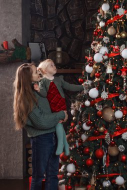 Anne ve küçük kızı Noel ağacının yanında kollarındaydılar. Anne ve küçük kız içeride Noel ağacı süsler. Dikey çerçeve