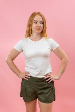 Beyaz tişörtlü ve şortlu ciddi bir yetişkin kadın portresi. Pembe arkaplan, dikey çerçeve.