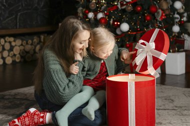 Küçük kız ve anne büyük bir hediye kutusunu hayranlıkla açıp içine bakın. Aile akşamı. Arka planda Noel ağacı