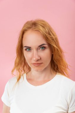 Kameraya bakan çekici genç bir kadının portresi. Yeşil gözlü ve kızıl saçlı bir kız. Pembe arkaplan, dikey çerçeve.