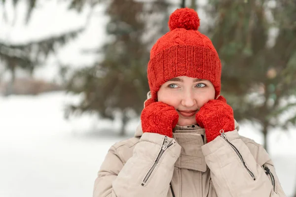 赤いニットミトンと帽子のかわいい女の子は 冬の森や公園の背景にポーズします 屋外で快適な冬服を着ている女性 — ストック写真