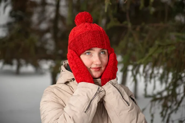 冬の森や公園の背景に編まれた赤い帽子とミトンのスタイリッシュなセットの美しい少女の肖像画 — ストック写真