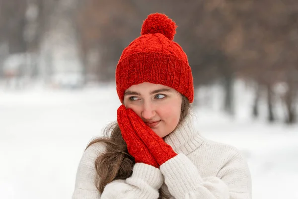 雪の公園で赤い帽子とミトンでかわいい若い女性 冬のアウトドアでブルネットガールの肖像画 ホリデイズ — ストック写真