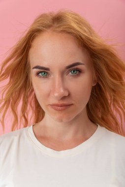 Doğrudan, kızıl saçlı, yeşil gözlü güzel bir kadının kamerasına bak. Pembe arka planda çekici bir genç kadın. Yakın çekim, dikey çerçeve.