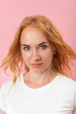 Kızıl saçlı, yeşil gözlü çekici bir kadının portresi. Çerçeveye bakan kendinden emin bir kadın. Pembe arkaplan, dikey çerçeve.