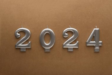 2024 yılının numaraları kahverengi arkaplandaki gümüş mumlardan yapılmış. Tatil geçmişi. Mutlu yıllar 2024. Yeni yılı kutluyoruz, yakın plan.