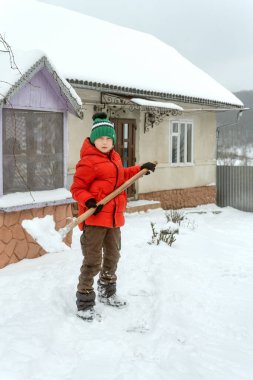 Kışın elinde kürekle evin bahçesinde kırmızı ceketli bir okul çocuğunun tam boy portresi. Dikey çerçeve