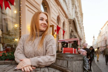Güzel sarışın kadın Noel tatilinde bir sokak kafesinde bir masada duruyor. Şehirde kış yürüyüşü.