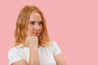 Çekici kadın düşünceli görünüyor. Pembe arkaplan, kopyalama alanı. Kızıl saçlı, yeşil gözlü bir kız..