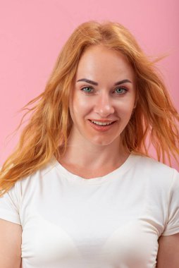 Kızıl saçlı, gülümseyen yuvarlak yüzlü bir kadının portresi. Pembe arka plandaki yeşil gözlü kız yan tarafa bakıyor