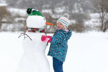 Küçük mutlu çocuk dışarıda büyük bir kardan adam yapıyor. Kardan adam çocuktan daha uzundur. Kış tatili
