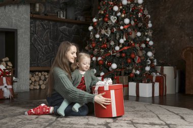 Anne ve küçük kız yılbaşı hediyelerinin tadını çıkarıyorlar Noel hediyelerini evde yeni yıl dekorasyonuyla birlikte evde tutuyorlar. Anne ve kızı Noel ağacının yanında.