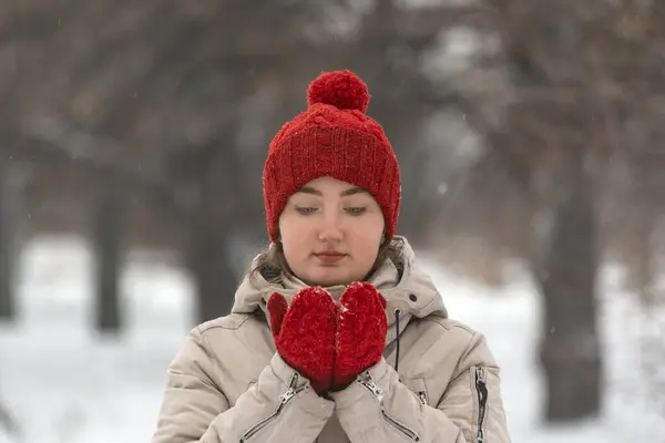Beautiful girl in wool red hat and mittens warms up in the winter outdoors. Woman in comfortable clothes for winter walks.
