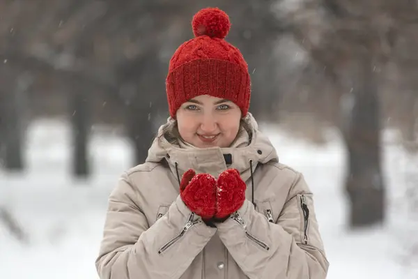 Attractive girl in wool red hat and mittens warms up in the winter outdoors. Woman in comfortable clothes for winter walks.