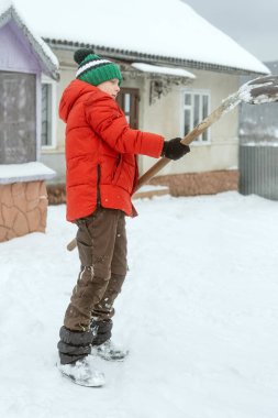 Evin kış bahçesinde elinde kürekle kırmızı ceketli bir öğrenci. Kış tatili Dikey çerçeve