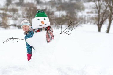 Mutlu çocuk kış yürüyüşünde kardan adamla oynuyor. Dışarıda kar figürü yapan bir çocuk var. Çocuklar için kış aktiviteleri