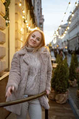 Şehir caddesinde kürklü gülümseyen sarışın bir kadının portresi. Akşam şenliği atmosferi. Dikey çerçeve.