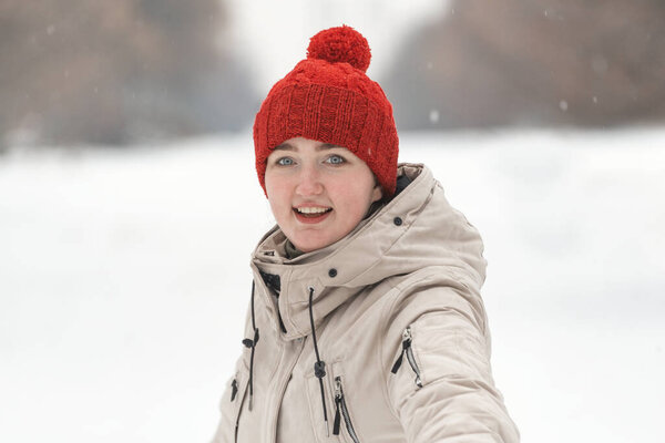 Portrait of happy girl in red knitted hat with bubo on snow park background. Woman in winter clothes in outside.