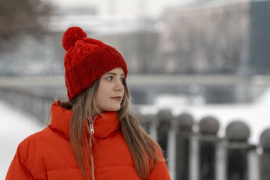 Uzun saçlı, kırmızı ceketli ve bubo şapkalı güzel esmer kız. Dışarıda şık kışlık giysiler içinde genç bir kadın var..